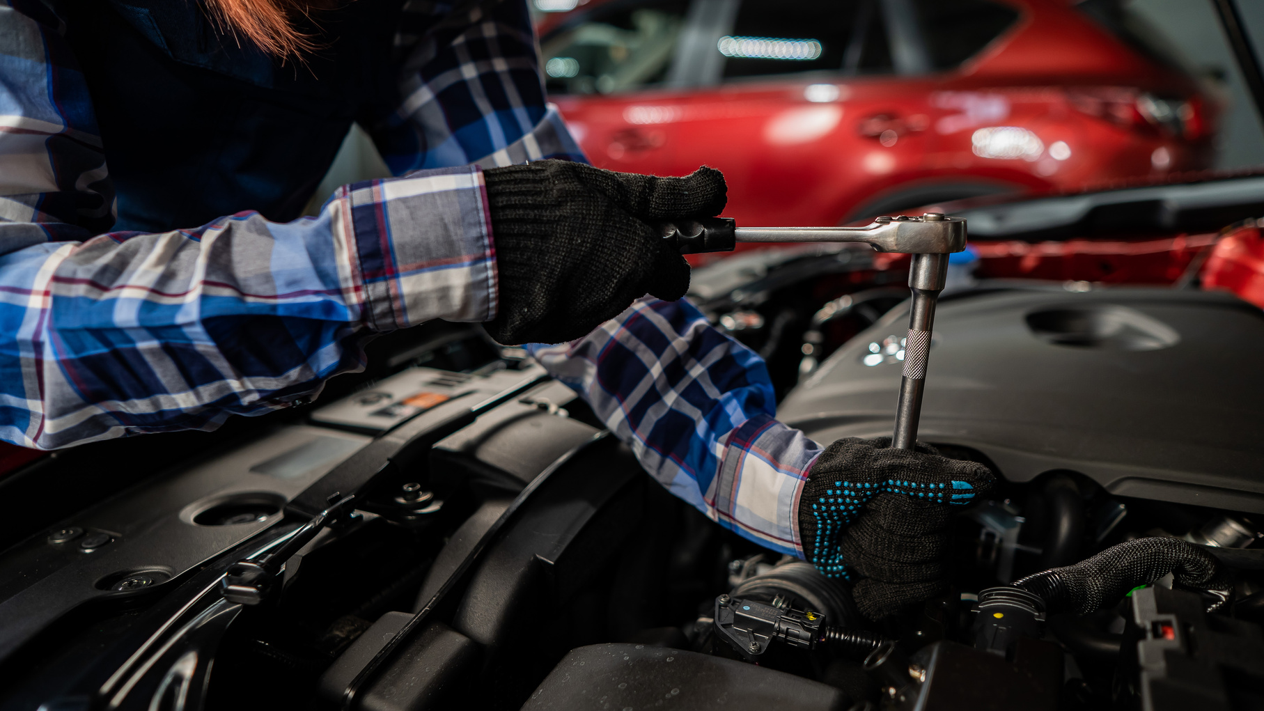 Female auto mechanic unscrewing a nut to replace a car spark plug.